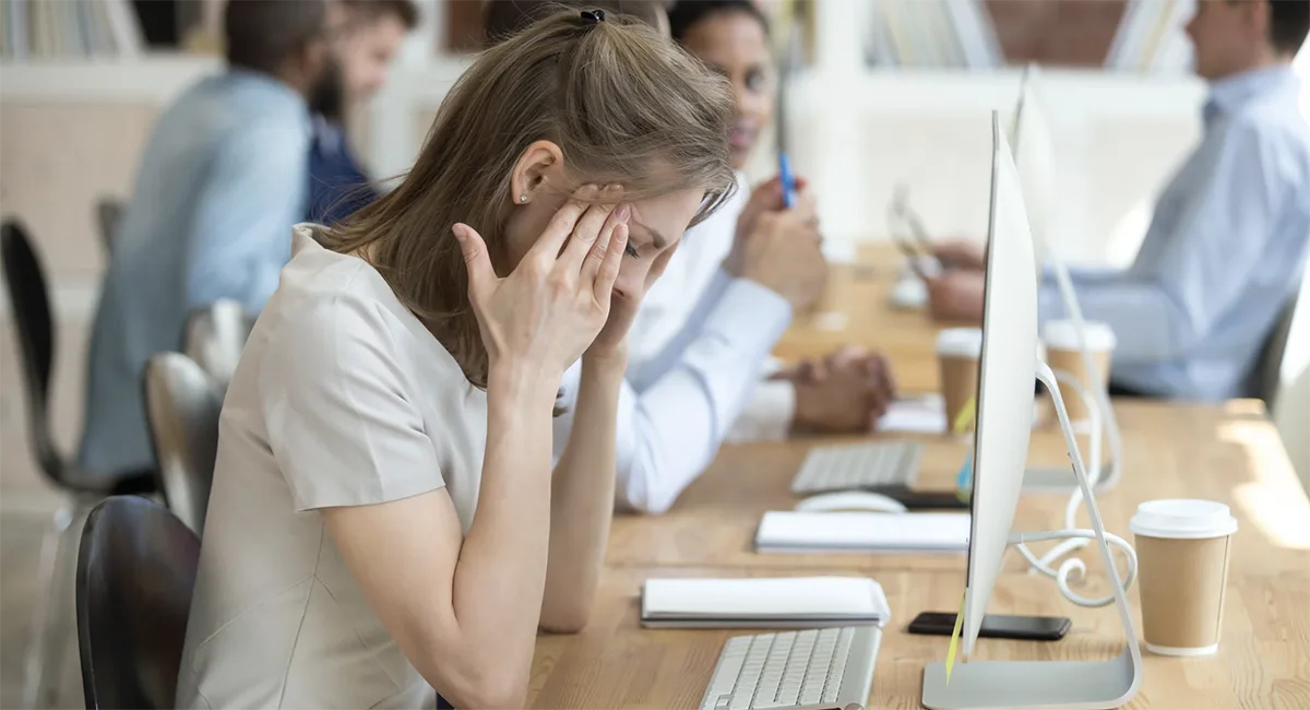 Office worker with headache in a modern workplace, possibly suffering from Sick Building Syndrome, highlighting the importance of indoor air quality and ergonomic office environments.